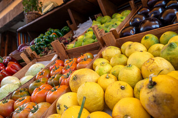 A variety of fruits and vegetables are displayed in a market. The produce includes tomatoes, lemons, and oranges