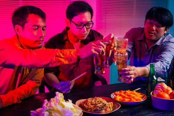 Three men are sitting at a table, holding glasses of beer and clinking glasses in celebration.They are enjoying food and drinks,eating and having fun in a party room with a happy,cheerful atmosphere