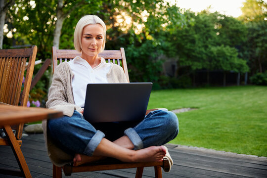 Mature woman using laptop in garden sitting on chair in backyard