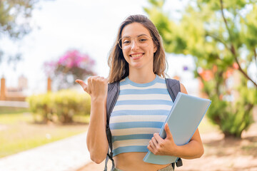 Young pretty student woman at outdoors pointing to the side to present a product