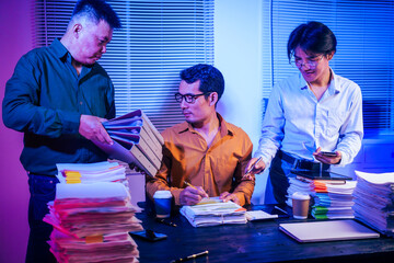 Three men work overtime at night, stressed and overloaded with tasks. They are exhausted, checking...