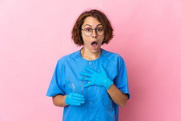 Woman English dentist holding tools over isolated on pink background surprised and shocked while looking right