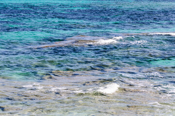 Texture of clear sea water with shades of turquoise and blue. The transparent water and gentle waves create a calming and visually appealing background, ideal for creative projects