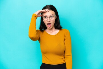 Young caucasian woman isolated on blue background doing surprise gesture while looking to the side