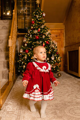 Little child dressed in a red velvet dress with white ruffles, standing thoughtfully in front of a...