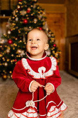A happy child in a red velvet dress with white ruffles holds a pearl bracelet while standing in...
