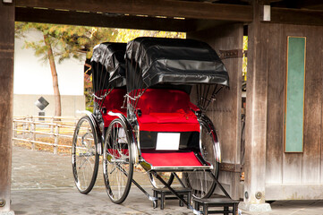 Red coloured seat rickshow parked under a wooden gate