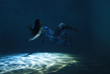 Fototapeta premium Beautiful woman in blue dress posing underwater as zero gravity in light beam