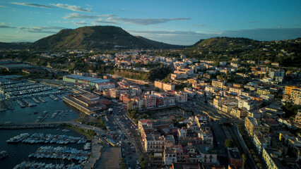Obraz premium A stunning aerial shot of Pozzuoli, highlighting its scenic coastline and vibrant harbor.The drone captures the ancient Roman ruins, the calm sea, and the natural beauty surrounding the historic city.