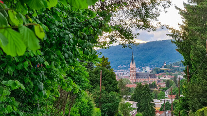 Tree branch framing distant view of majestic church Herz Jesu Kirche in Graz, Styria, Austria. Landmark against dramatic sky. Intricate architectural details, including pointed spire, ornate windows