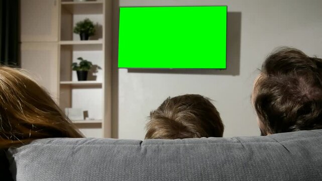 A happy family watching TV with chromakey screen sitting on a sofa in the evening