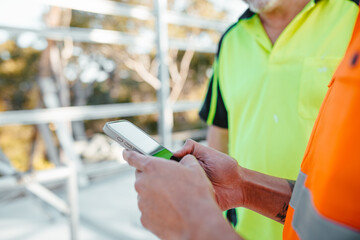 Construction worker holding a mobile device at the construction site.