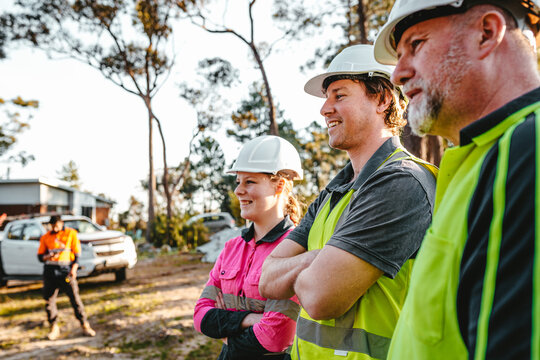 Three construction workers standing on worksite with arms crossed.