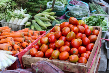 Basket filled with tomatoes, carrots, radishes, corn, and the green vegetable at fresh market.