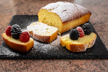 Close-up on the homemade plum cake resting on a black stone cutting board while being dusted with icing sugar. Cooking at home. Delicious healthy homemade dessert served with berries