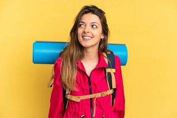 Young mountaineer man with a big backpack isolated on yellow background thinking an idea while looking up