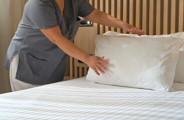Cleaning staff carefully adjusting pillows on a bed in a neat hotel room with wooden decor, showcasing attention to detail.