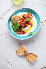 Bowl of ricotta dip with chopped tomatoes and ciabatta, vertical shot on a white granite background, above view