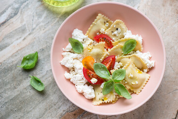 Italian ravioli served with ricotta, tomatoes and basil, horizontal shot on a grey and roseate granite background, elevated view