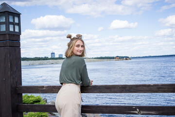 young blond woman in a sweater, portrait, standing on a bridge on the lake, smiling, posing, photosession
