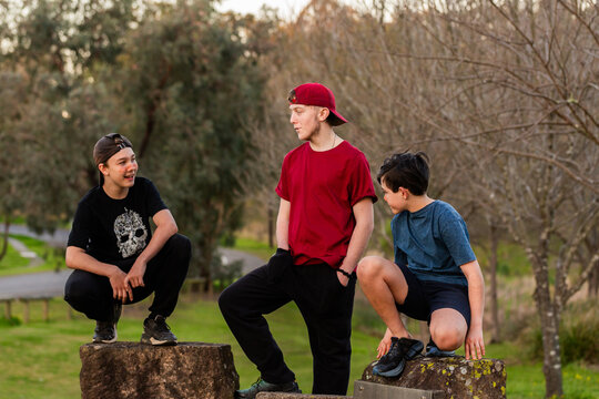 Teenaged and pre teen boys crouched on rocks at park chatting