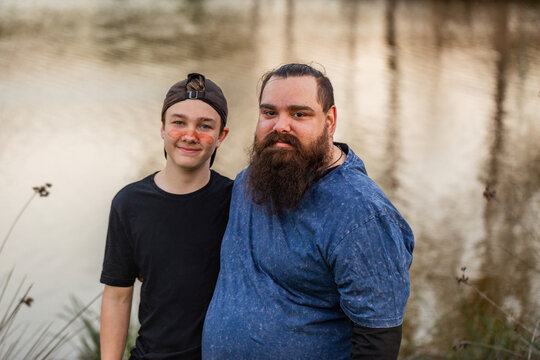 Aboriginal boy and father standing together by waterside at dusk