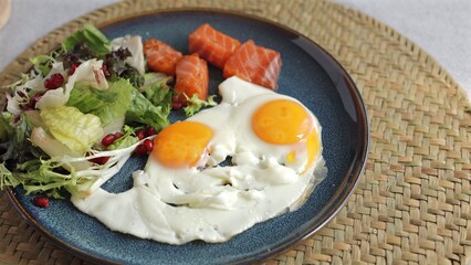 Vibrant sunny-side-up eggs, fresh salad, and salmon slices on blue plate reflect balanced eco-friendly breakfast focused on nutritious, wellness-focused clean eating.