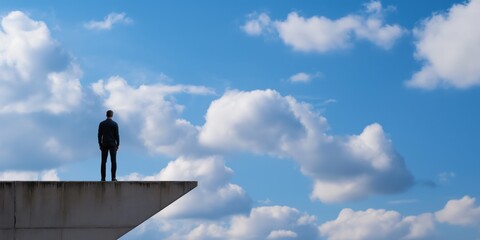 A man stands on the edge of a building, silhouetted against a vast cloudy sky, exemplifying feelings of solitude, ambition, and contemplating future possibilities.