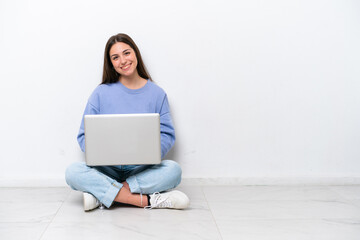 Young caucasian woman with laptop sitting on the floor isolated on white background with arms...