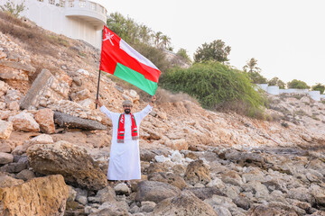 Omani man holding omani flag with two hand at the beach