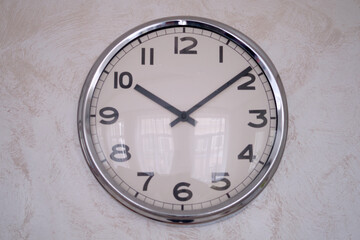 A large round clock with a black dial on the wall. Big white wall clock with hands and numbers.