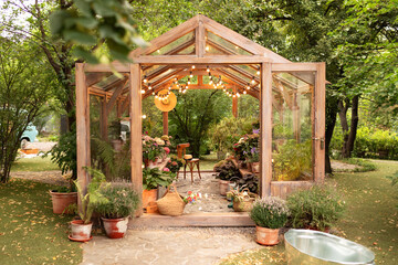 Interior of a wooden illuminated greenhouse with furniture, plants and flowers in pots at backyard....
