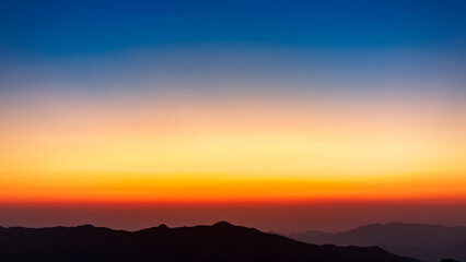 The sky gradient from blue to orange over the mountains. The mountains look like an oriental painting.