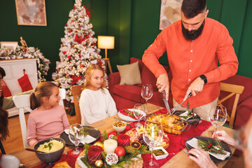 Family having Christmas dinner at home, man cutting chicken