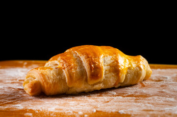 A fresh croissant with a golden, crispy crust and flaky texture lies on a wooden board. Organic baking