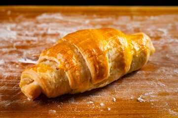 A fresh croissant with a golden, crispy crust and flaky texture lies on a wooden board. Organic baking