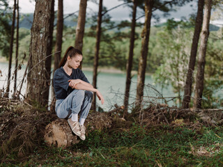 Thoughtful young woman sitting on a rock in a forest, surrounded by trees near water Relaxation and nature connection concept Emotions of contemplation and peace