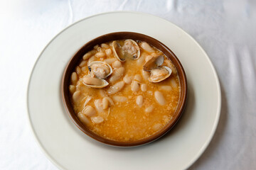 Casserole of beans with clams on a white plate on a white tablecloth
