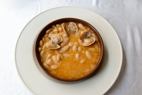 Casserole of beans with clams on a white plate on a white tablecloth