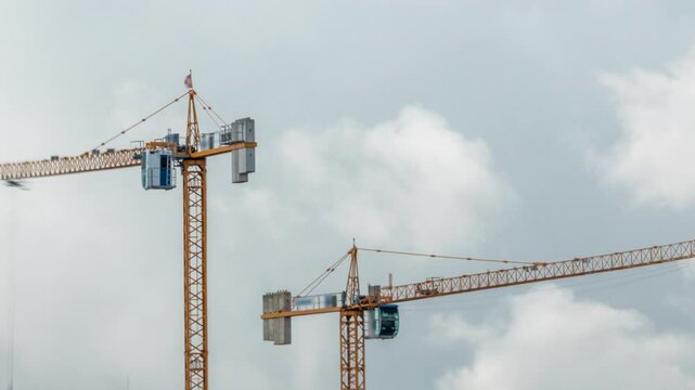 Big construction site including several cranes working and moving on a building complex, with cloudy sky timelapse. Massive clouds passing by