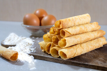 A stack of freshly baked Egg Roll cookies or biscuits displayed with flour and eggs, highlighting homemade baking with simple ingredients. Perfect for a cozy dessert or snack idea.