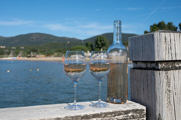 Bottle and glass of cold rose wine from Provence and wooden yacht boota pier on white sandy beach Plage de Pampelonne near Saint-Tropez, summer vacation in France