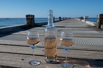 Tasting of cold rose wine from Provence outdoor on wooden yacht pier with view on blue water and white sandy beach Plage de Pampelonne near Saint-Tropez, summer vacation in France