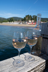 Bottle and glass of cold rose wine from Provence and wooden yacht boota pier on white sandy beach Plage de Pampelonne near Saint-Tropez, summer vacation in France