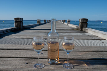 Tasting of cold rose wine from Provence outdoor on wooden yacht pier with view on blue water and white sandy beach Plage de Pampelonne near Saint-Tropez, summer vacation in France