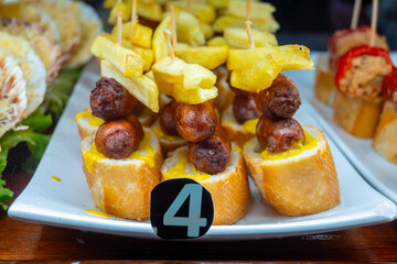 Typical snacks of Basque Country, variety of pinchos or pinxtos oven baked sea food, bread, skewers with jamon, goat cheese served in bar in San-Sebastian or Bilbao, Spain, close up