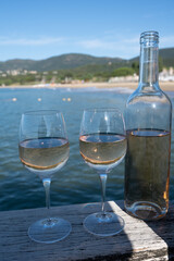Bottle and glass of cold rose wine from Provence and wooden yacht boota pier on white sandy beach Plage de Pampelonne near Saint-Tropez, summer vacation in France