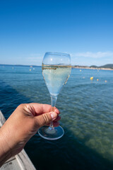 Summer time in Provence, hand with glass of cold champagne cremant sparkling wine on famous Pampelonne sandy beach near Saint-Tropez in sunny day, Var department, France, beach club party