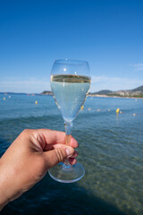 Summer time in Provence, hand with glass of cold champagne cremant sparkling wine on famous Pampelonne sandy beach near Saint-Tropez in sunny day, Var department, France, beach club party