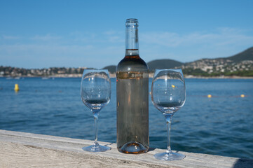 Obraz premium Tasting of cold rose wine from Provence outdoor on wooden yacht pier with view on blue water and white sandy beach Plage de Pampelonne near Saint-Tropez, summer vacation in France
